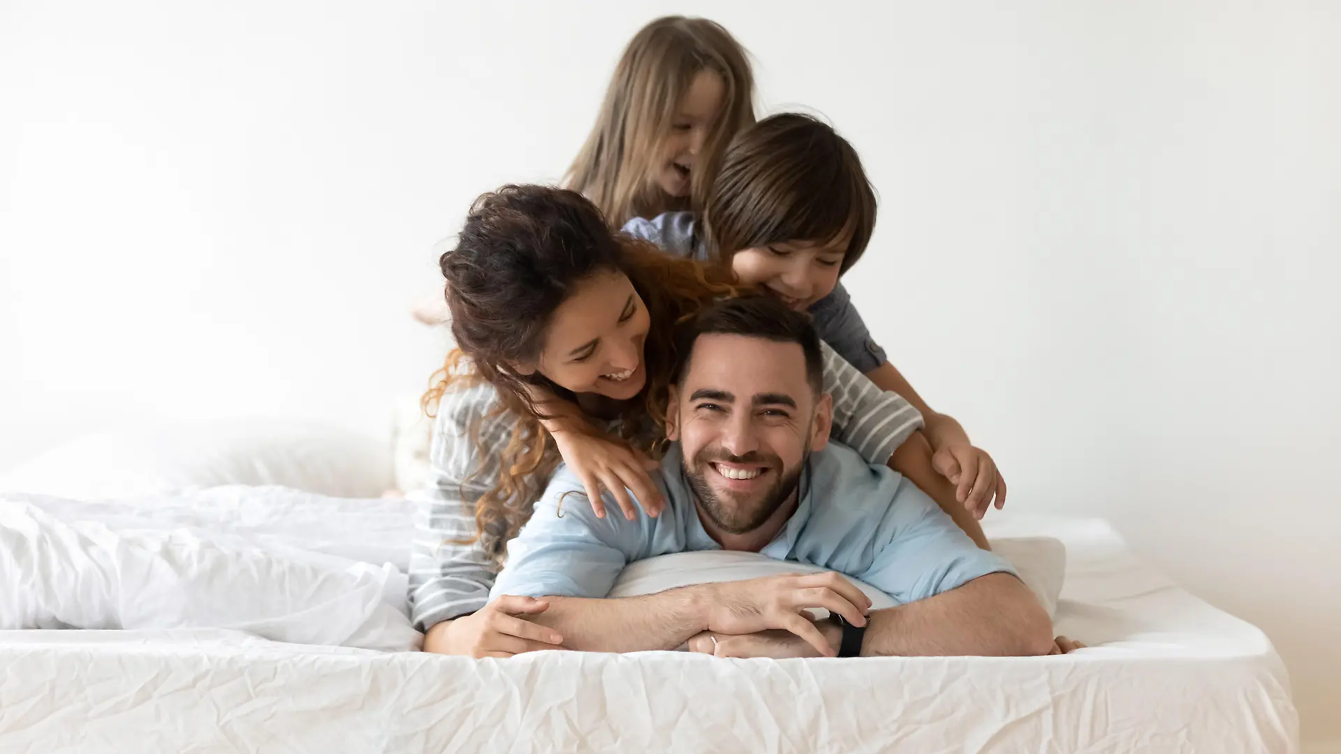 Portrait of happy young parents and small preschooler kids lying on white mattress in bedroom look at camera together, smiling family with little children relax on bed have fun, furniture concept
