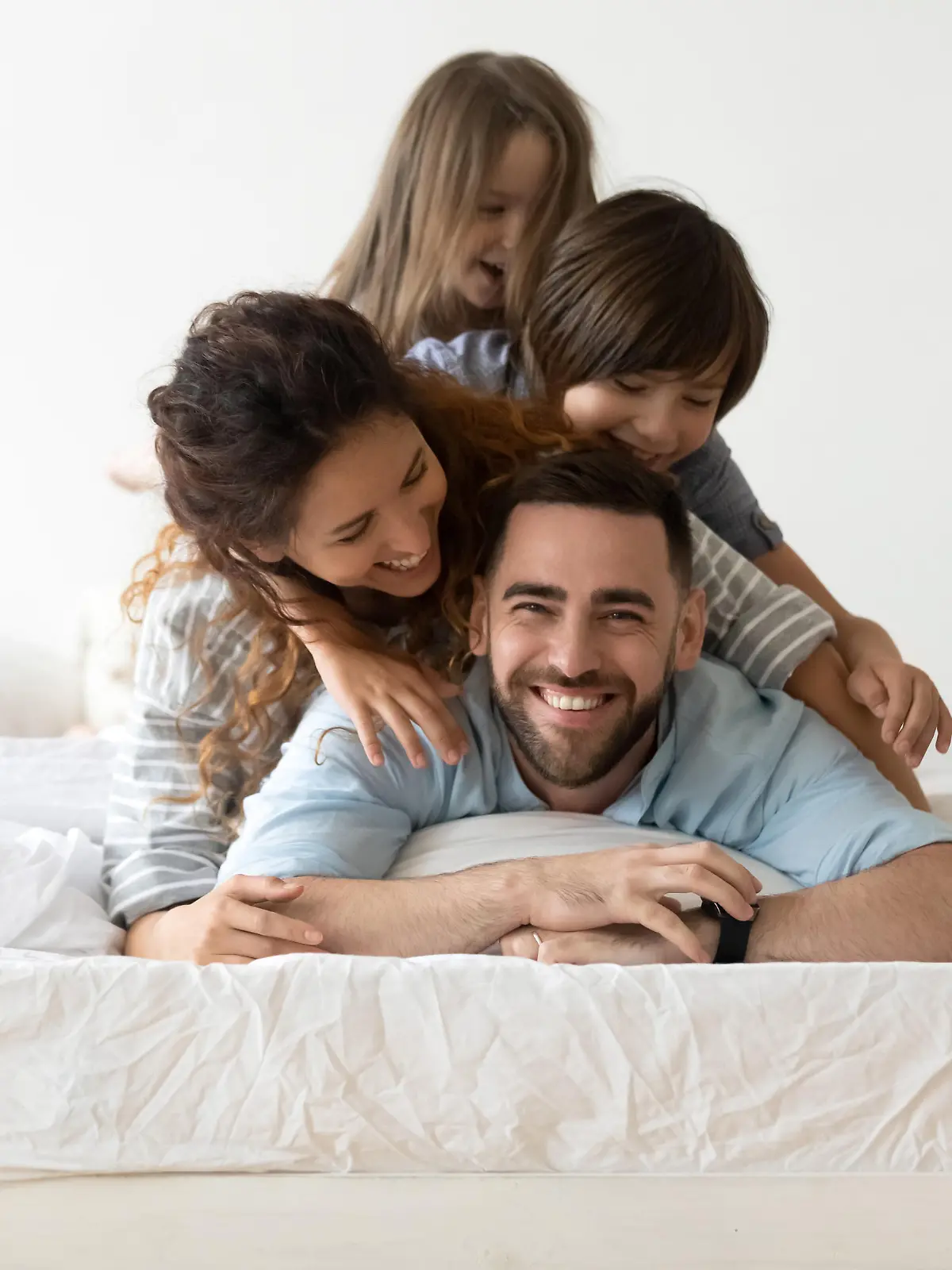 Portrait of happy young parents and small preschooler kids lying on white mattress in bedroom look at camera together, smiling family with little children relax on bed have fun, furniture concept