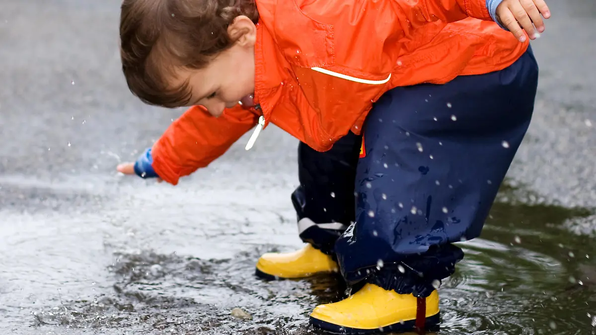 Little Boy having fun with a puddle after the rainfall and sticking out his tongue out of joy (unfortunately hidden by watermark).