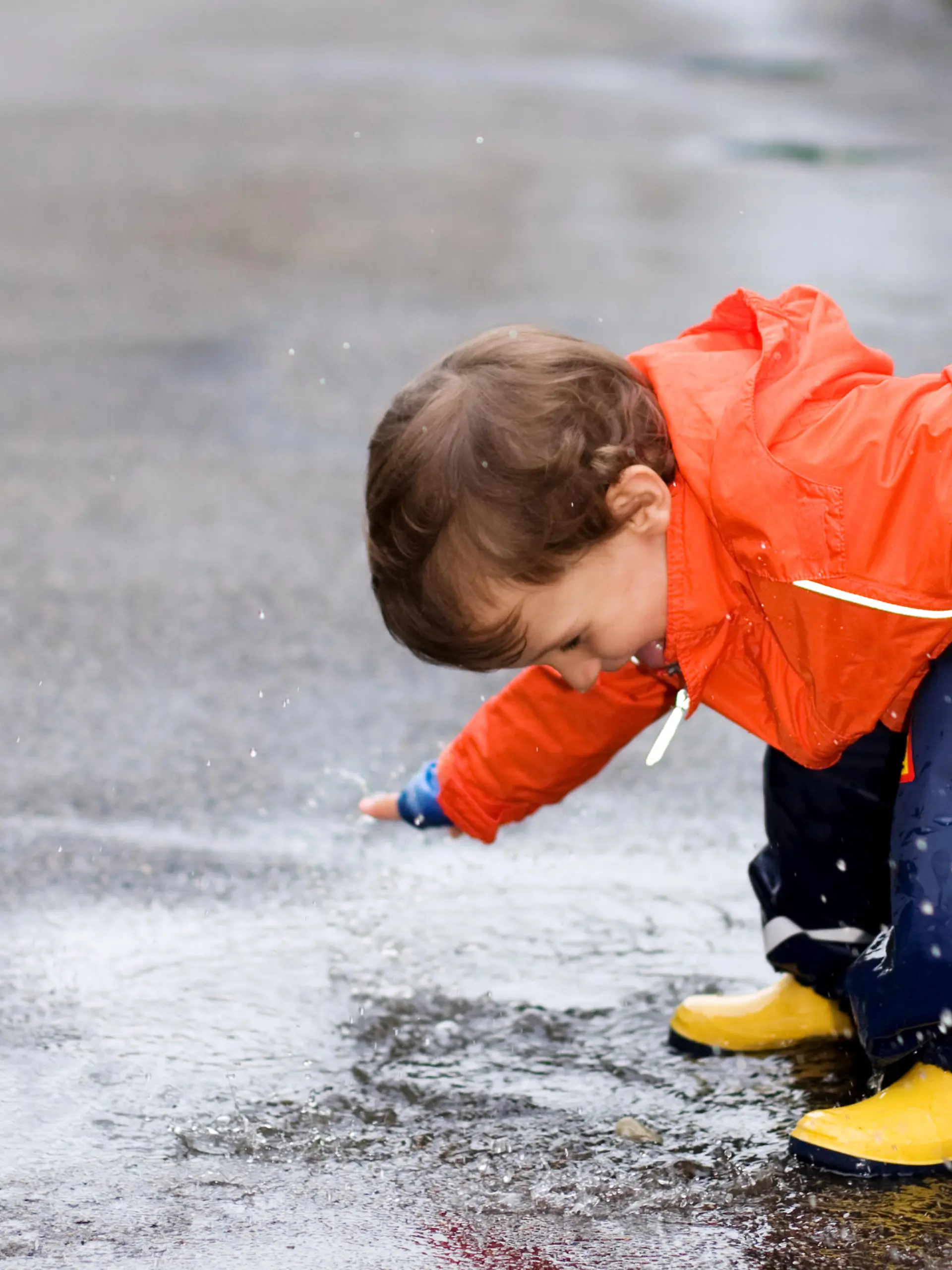 Little Boy having fun with a puddle after the rainfall and sticking out his tongue out of joy (unfortunately hidden by watermark).