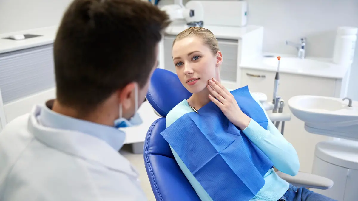 people, medicine, stomatology and health care concept - woman patient talking to male dentist and complain of toothache at dental clinic office