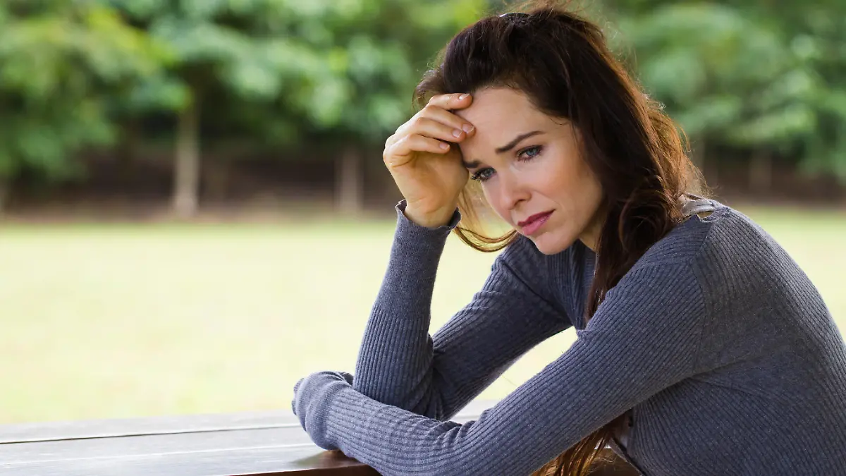 A sad and worried woman sitting down alone outdoors