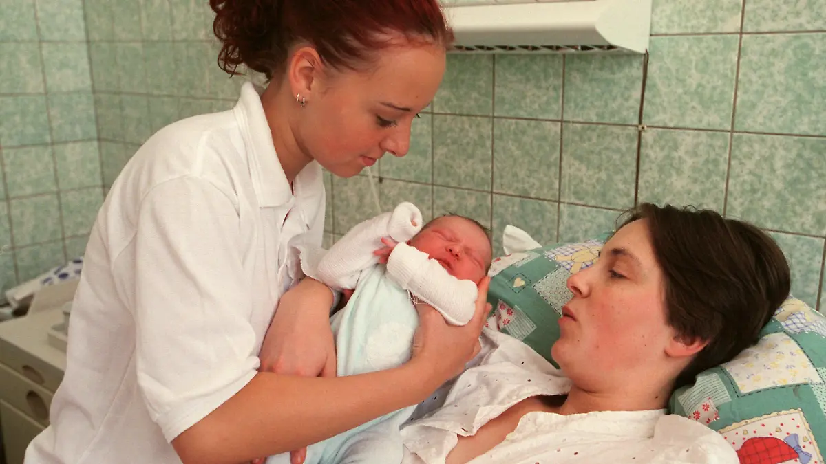 Leipzig (Sachsen): Hebammenschülerin Patricia Brodalla (17) reicht der jungen Mutter Ariane Baby Lina eine Stune nach der Geburt in der Universitätsfrauenklinik Leipzig zu. In der Medizinischen Berufsfachschule der Klinik werden die Hebammenschülerinnen im Rahmen ihrer praktischen Ausbildung in alle erforderlichen Tätigkeiten im Zusammenhang mit Schwangerschaft und Geburt unter Anleitung von Fachkräften einbezogen. Die angehenden Hebammen erhalten eine dreijährige Ausbildung in fachbezogenen naturwissenschaftlichen und geburtshilflichen Fächern sowie medizinischen Grundlagenfächern, die zu einem Abschluss mit Berufserlaubnis führt. Die Schule, eine von über 50 Hebammenschulen in Deutschland, besteht seit 1810. Jährlich bewerben sich hier zwischen 600 und 700 interessierte Jugendliche aus der gesamten Bundesrepublik.  (LEI409-111200)