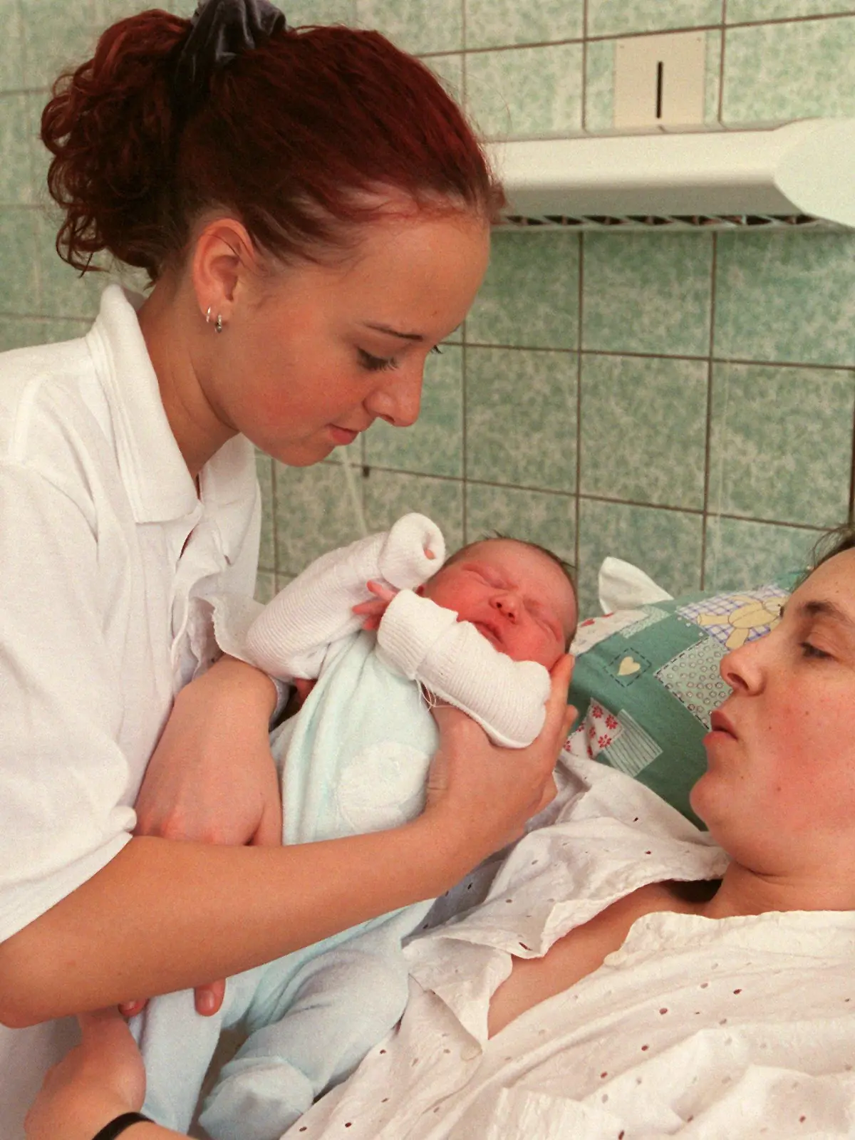 Leipzig (Sachsen): Hebammenschülerin Patricia Brodalla (17) reicht der jungen Mutter Ariane Baby Lina eine Stune nach der Geburt in der Universitätsfrauenklinik Leipzig zu. In der Medizinischen Berufsfachschule der Klinik werden die Hebammenschülerinnen im Rahmen ihrer praktischen Ausbildung in alle erforderlichen Tätigkeiten im Zusammenhang mit Schwangerschaft und Geburt unter Anleitung von Fachkräften einbezogen. Die angehenden Hebammen erhalten eine dreijährige Ausbildung in fachbezogenen naturwissenschaftlichen und geburtshilflichen Fächern sowie medizinischen Grundlagenfächern, die zu einem Abschluss mit Berufserlaubnis führt. Die Schule, eine von über 50 Hebammenschulen in Deutschland, besteht seit 1810. Jährlich bewerben sich hier zwischen 600 und 700 interessierte Jugendliche aus der gesamten Bundesrepublik.  (LEI409-111200)