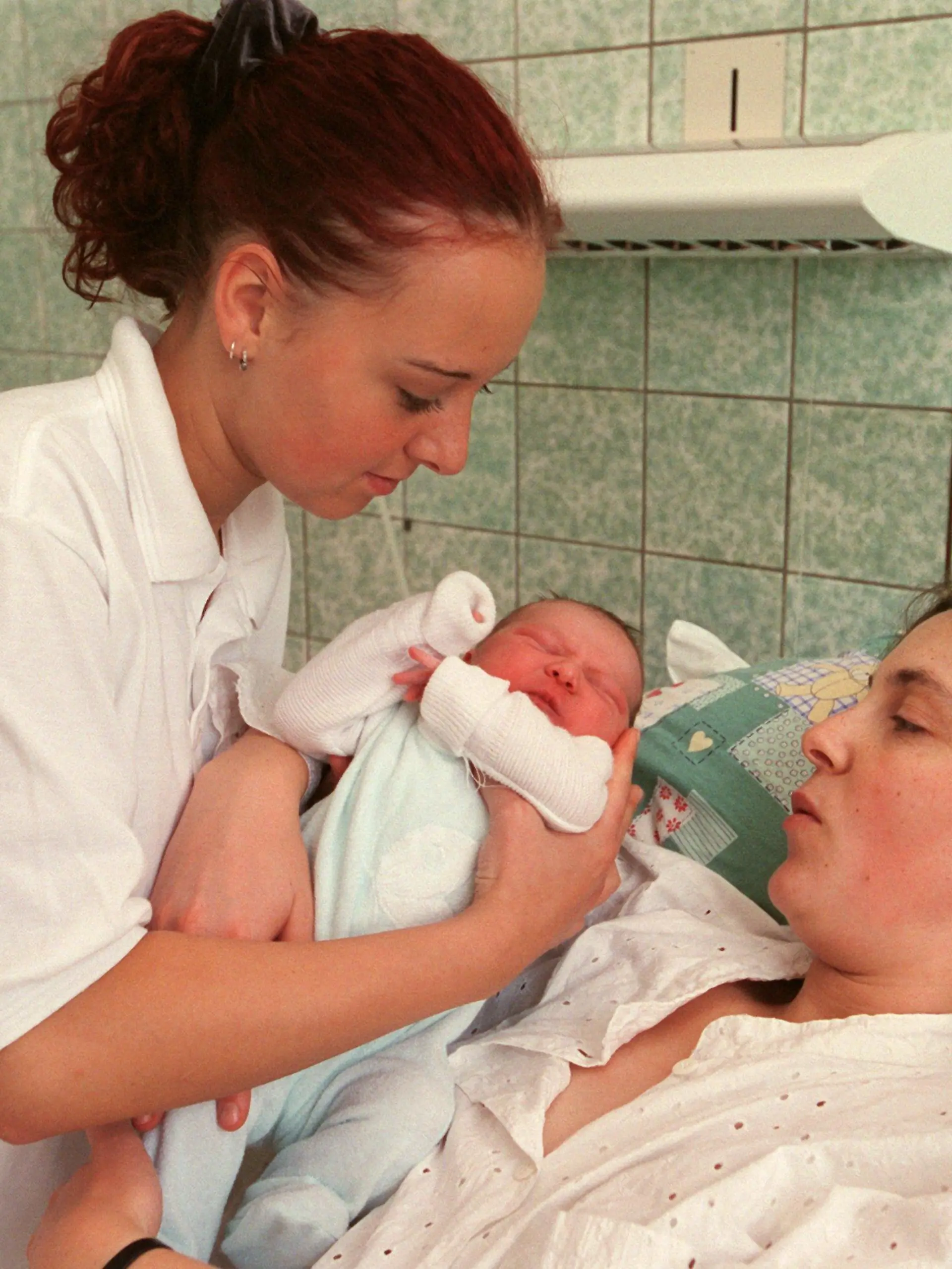Leipzig (Sachsen): Hebammenschülerin Patricia Brodalla (17) reicht der jungen Mutter Ariane Baby Lina eine Stune nach der Geburt in der Universitätsfrauenklinik Leipzig zu. In der Medizinischen Berufsfachschule der Klinik werden die Hebammenschülerinnen im Rahmen ihrer praktischen Ausbildung in alle erforderlichen Tätigkeiten im Zusammenhang mit Schwangerschaft und Geburt unter Anleitung von Fachkräften einbezogen. Die angehenden Hebammen erhalten eine dreijährige Ausbildung in fachbezogenen naturwissenschaftlichen und geburtshilflichen Fächern sowie medizinischen Grundlagenfächern, die zu einem Abschluss mit Berufserlaubnis führt. Die Schule, eine von über 50 Hebammenschulen in Deutschland, besteht seit 1810. Jährlich bewerben sich hier zwischen 600 und 700 interessierte Jugendliche aus der gesamten Bundesrepublik.  (LEI409-111200)
