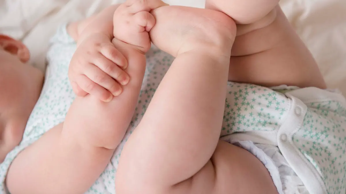Baby girl (12-17 months) lying down with hands on feet, Baby (12-17 Monate) liegend mit den Haenden an den Fuessen || Modellfreigabe vorhanden