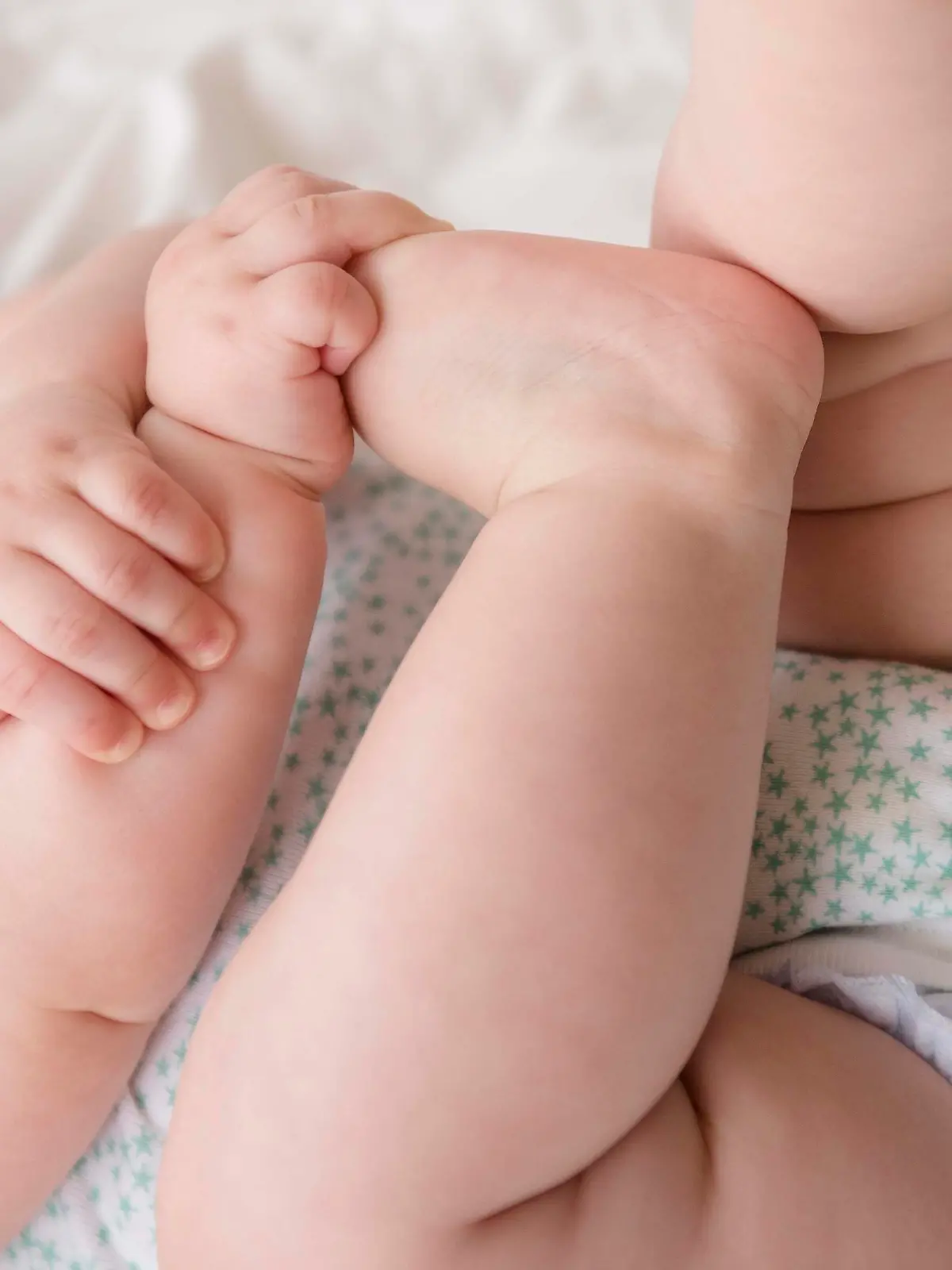 Baby girl (12-17 months) lying down with hands on feet, Baby (12-17 Monate) liegend mit den Haenden an den Fuessen || Modellfreigabe vorhanden