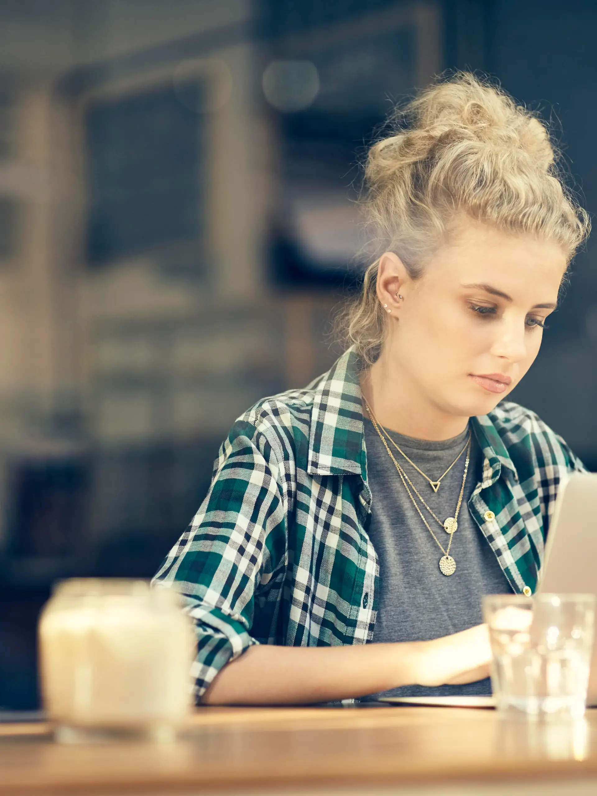 A photo of beautiful young woman using laptop at table inside cafe window. Female customer sitting in coffee shop. She is in trendy casuals.