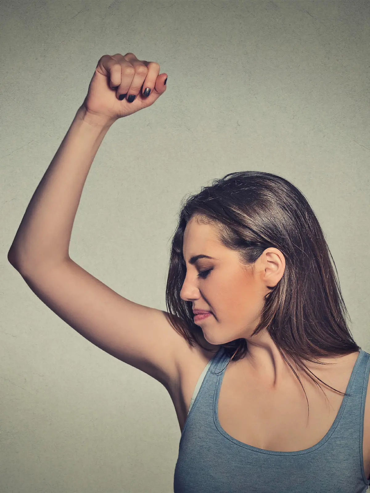 Closeup portrait young woman, smelling, sniffing her wet armpit, something stinks, very bad foul odor situation isolated grey wall background. Negative human emotion facial expression feeling reaction