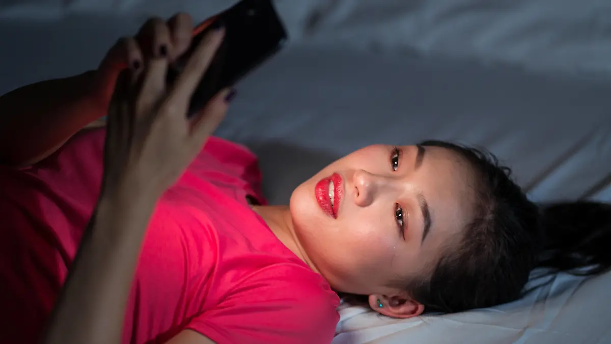 From above ethnic woman smiling and browsing dating app on smartphone while lying on bed in evening at home Copyright: xJuanxAlbertoxRuizx