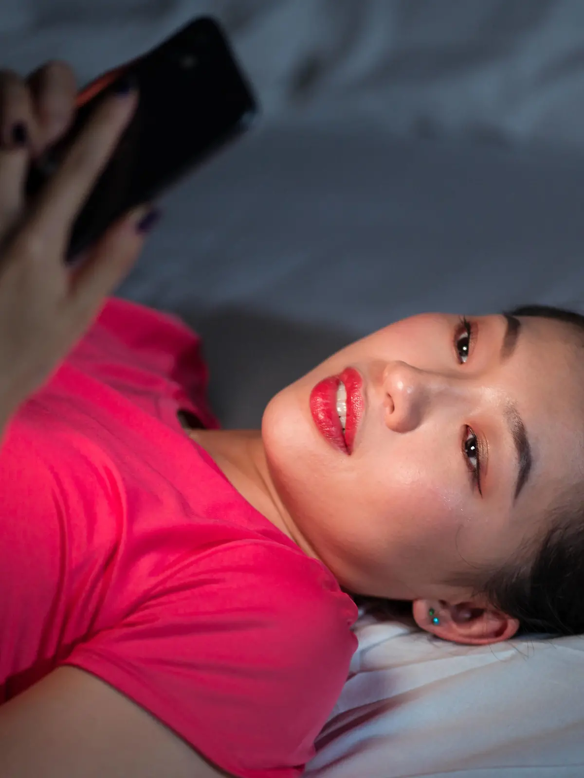 From above ethnic woman smiling and browsing dating app on smartphone while lying on bed in evening at home Copyright: xJuanxAlbertoxRuizx