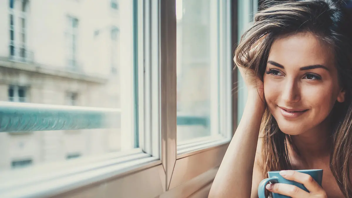 Beautiful young woman holding a cup of coffee looking through a house window. Shot made during Istockalypse Paris 2016 event.