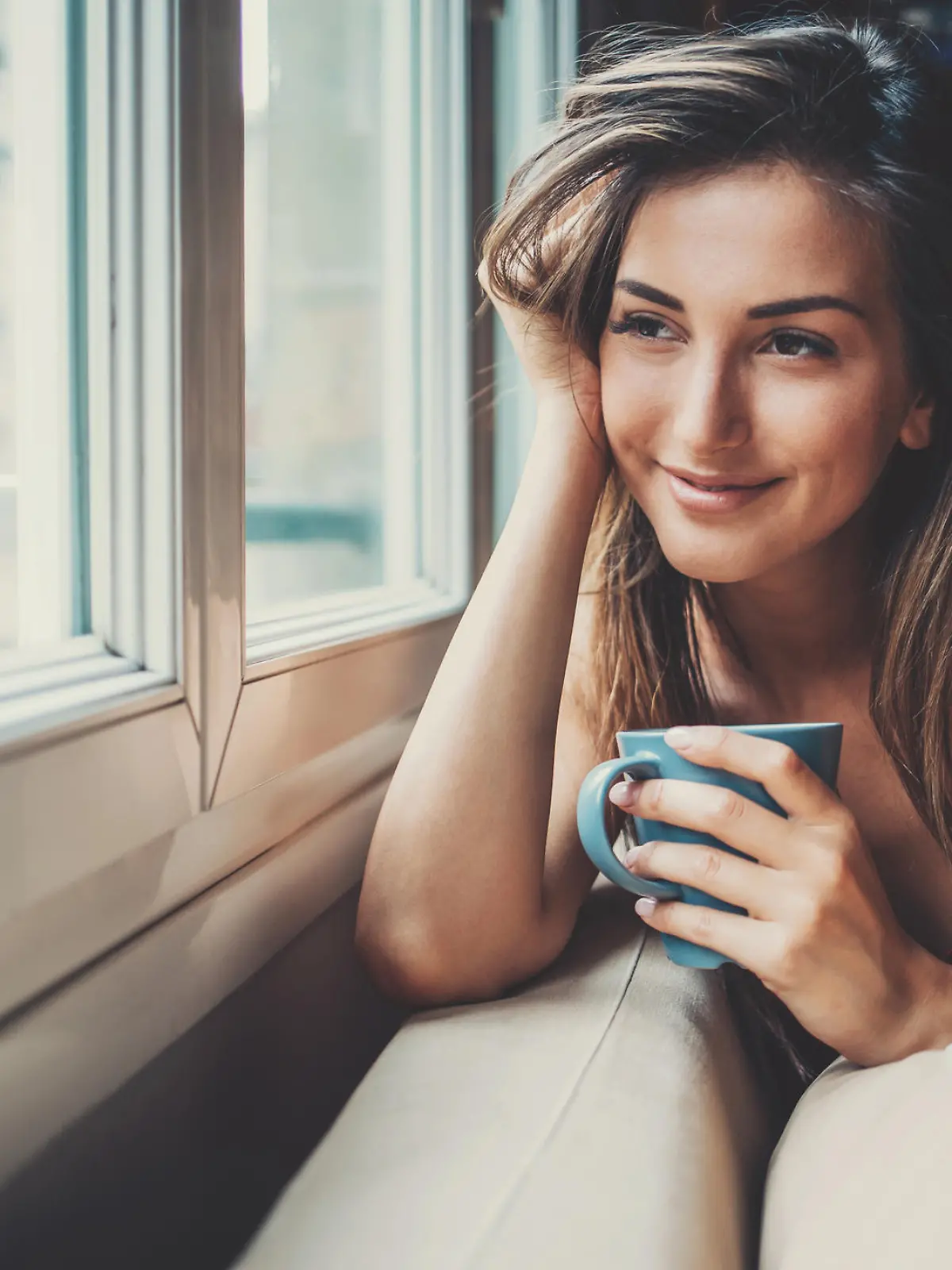 Beautiful young woman holding a cup of coffee looking through a house window. Shot made during Istockalypse Paris 2016 event.