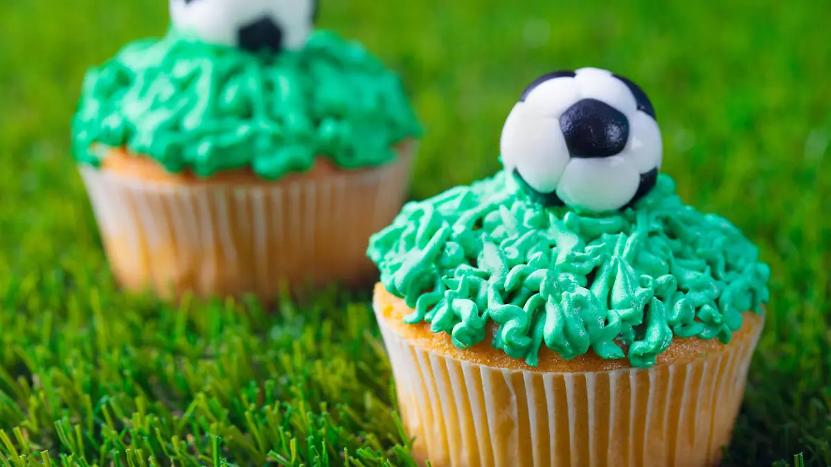 Football party, birthday decorated cupcake on green grass background. Close up