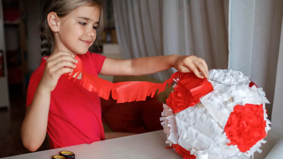 Preteen girl doing pinata with cardboard from used box and color crepe paper, decorated container filled with candy as a part of celebration, diy decoration at birthday, soccer party