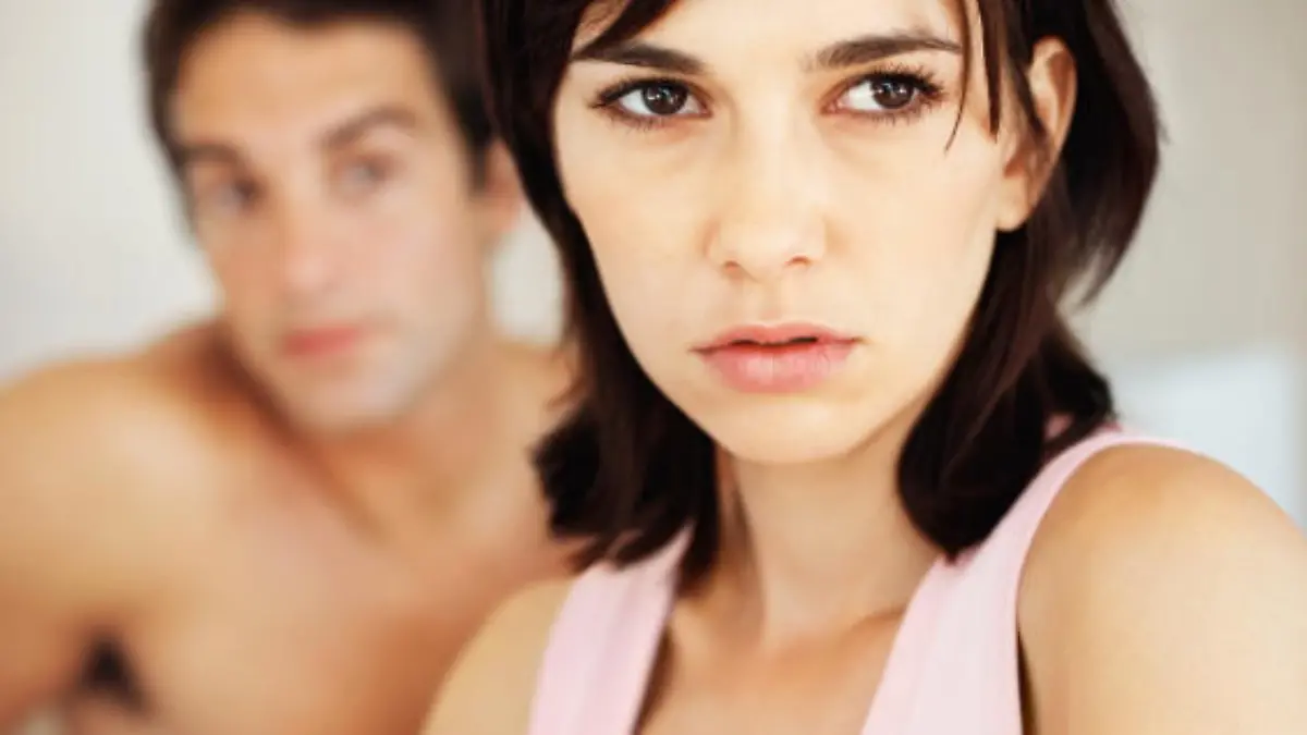 Portrait of a upset young woman sitting on bed with a man in background