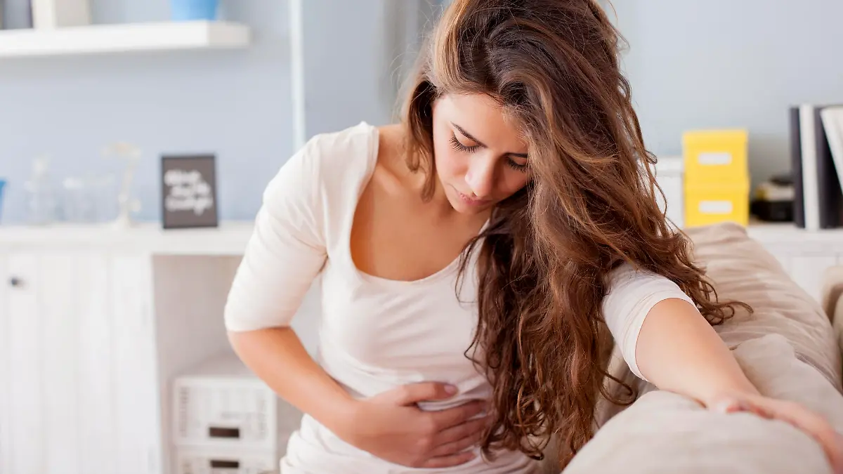 Junge Frau auf Sofa hält sich den Bauch vor Schmerzen oder Übelkeit