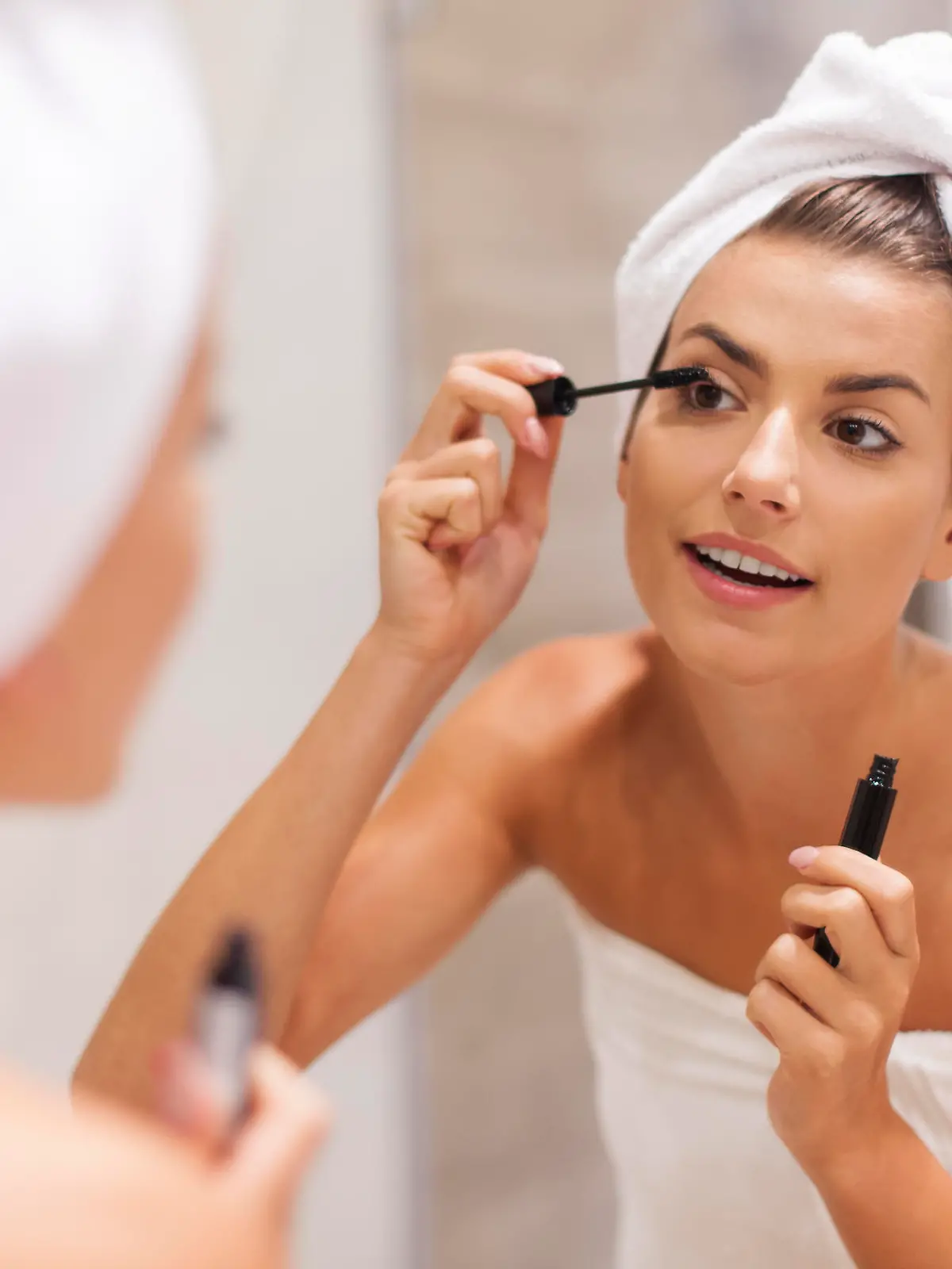 Beautiful woman using mascara in bathroom