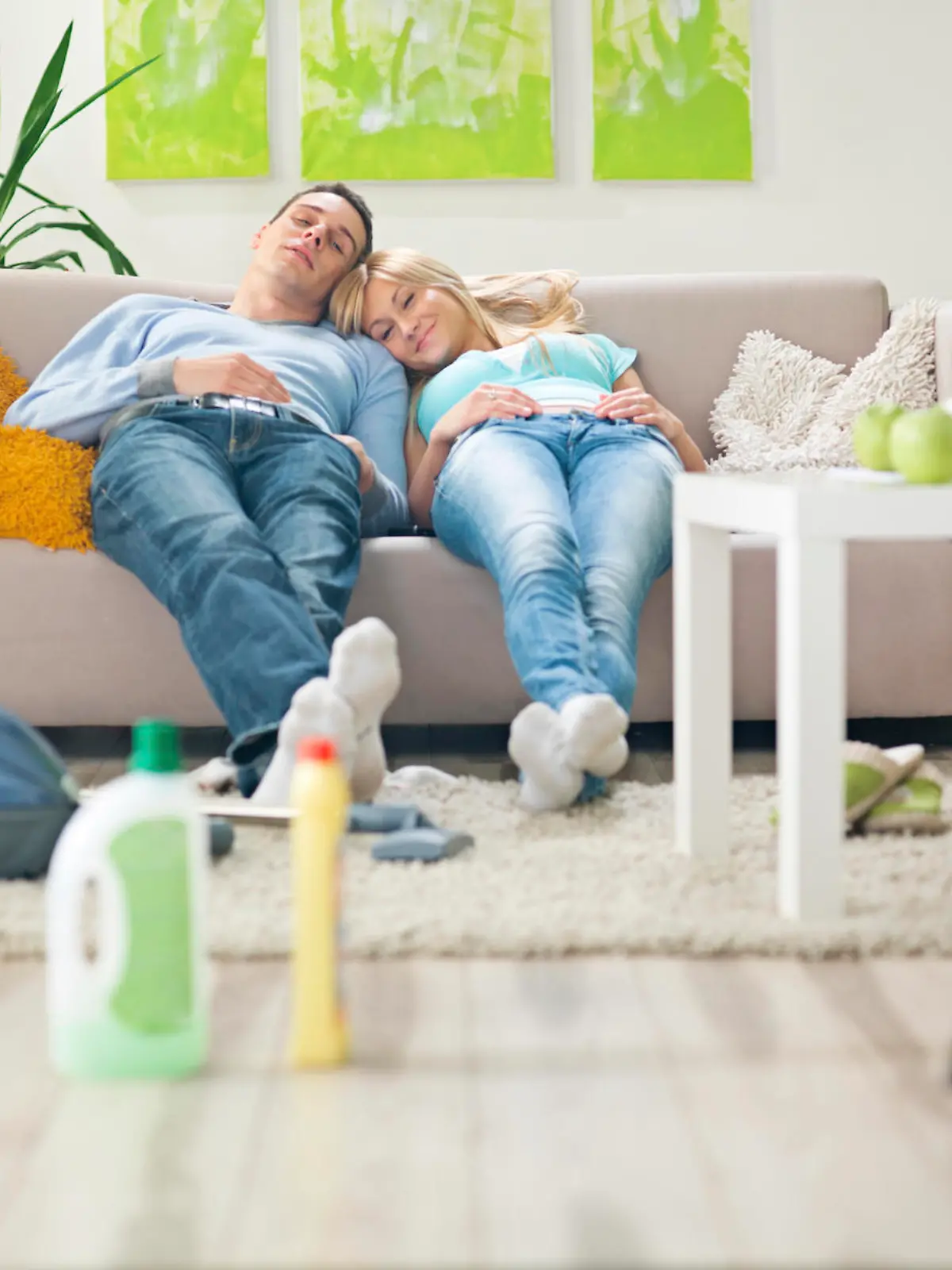 Young couple in brightly lit contemporary living room resting on sofa after cleaning  the room