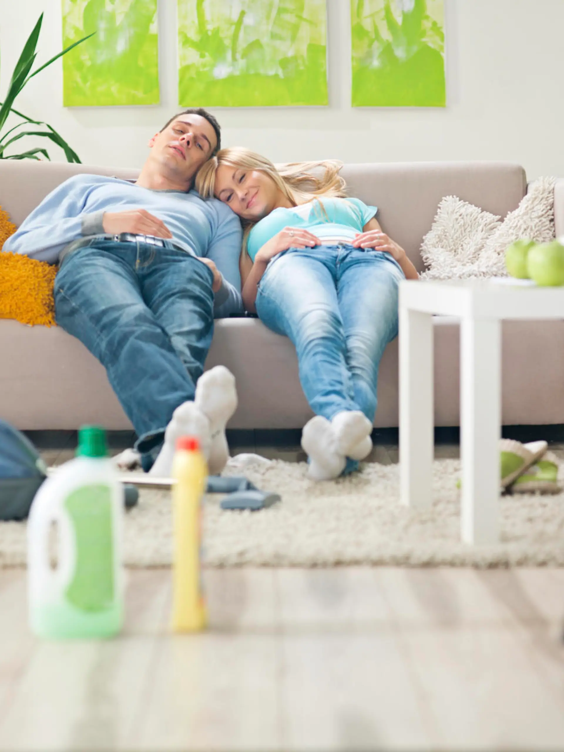 Young couple in brightly lit contemporary living room resting on sofa after cleaning  the room