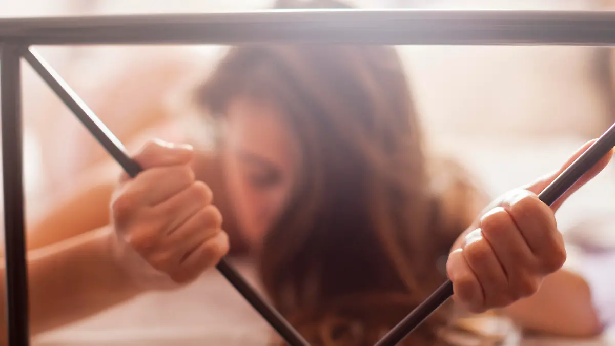Sexy woman lying naked in bed in the bedroom. She is enjoying in sexual games and during orgasm she squeezes the rod on the bed with great passion. Very shallow depth of field with focus on her left hand