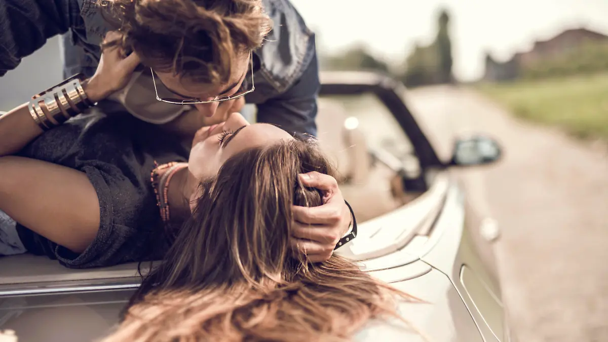 Young loving couple having a desire toward each other while lying on cabriolet.