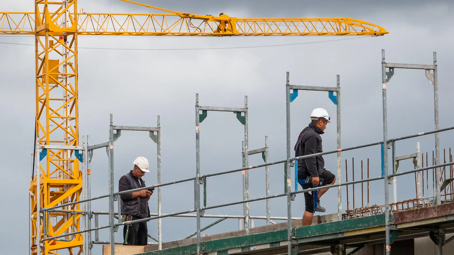 08.07.2019, Niedersachsen, Hannover: Zwei Bauarbeiter gehen auf einer Baustelle auf einem Hausdach auf dem Gerüst. Bauminister Lies (SPD) hat am Montag (08.07.2019) die Ergebnisse des Wohnungsmarktberichts 2018/19 für Niedersachsen vorgestellt. Foto: Cindy Riechau/dpa +++ dpa-Bildfunk +++