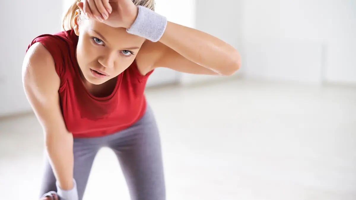 Tired woman wiping sweat off forehead after workout