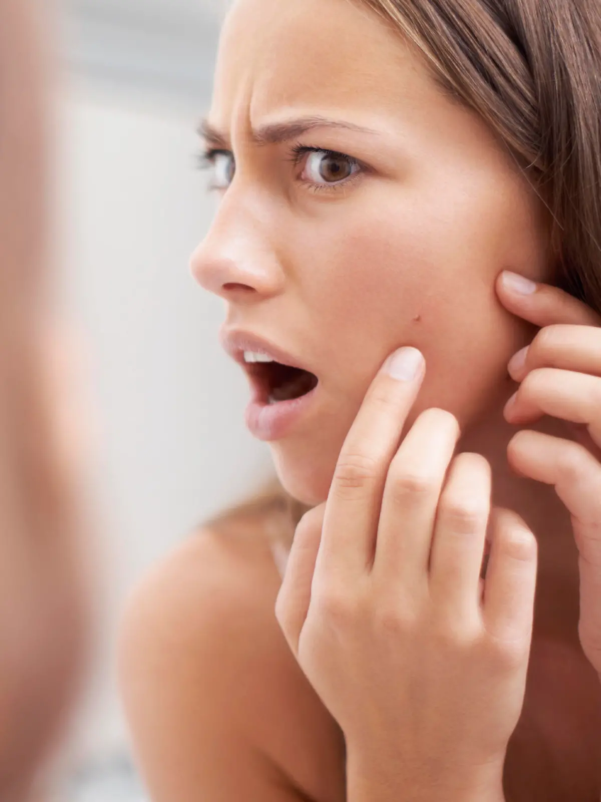 A young woman looking shocked as she examines her skin