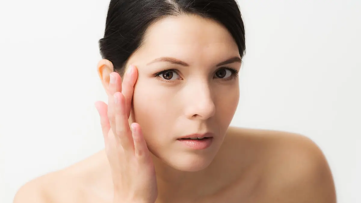 Portrait of a sexy brunette Caucasian young woman looking in the mirror, observing facial wrinkles, first sign of ageing