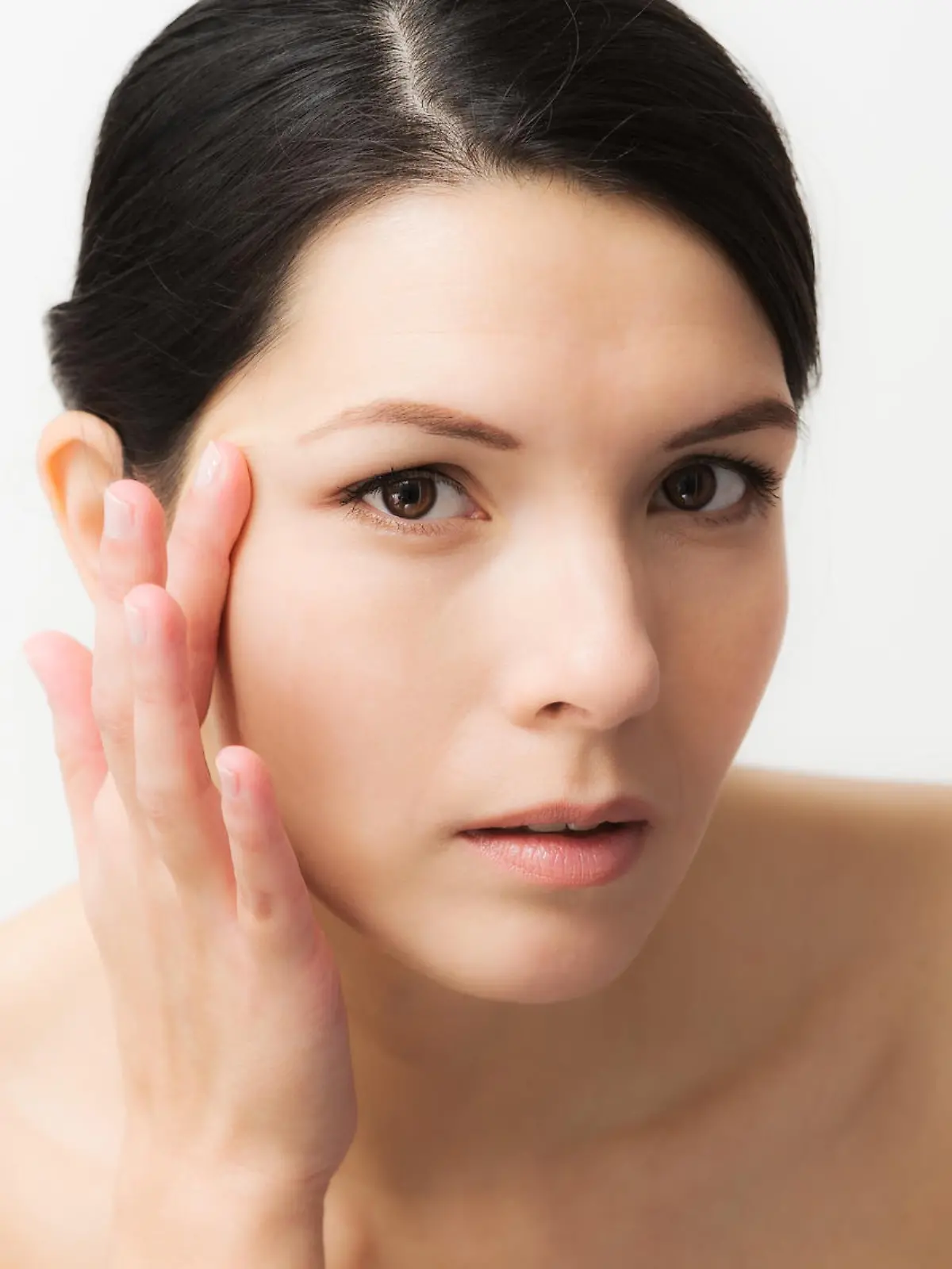 Portrait of a sexy brunette Caucasian young woman looking in the mirror, observing facial wrinkles, first sign of ageing