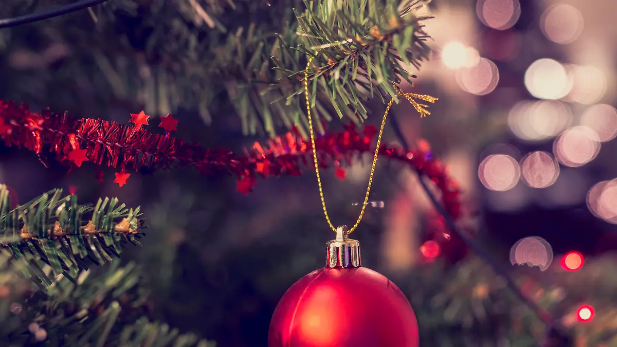 Closeup of red bauble hanging from a decorated Christmas tree. Retro filter effect.
