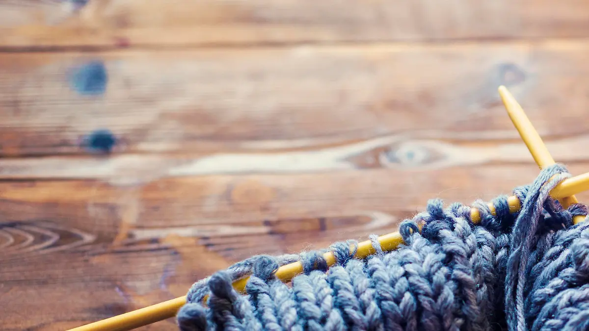 view from above on a wooden table with lots of balls of wool, knitting needles and other tools. Place for text and the word craft