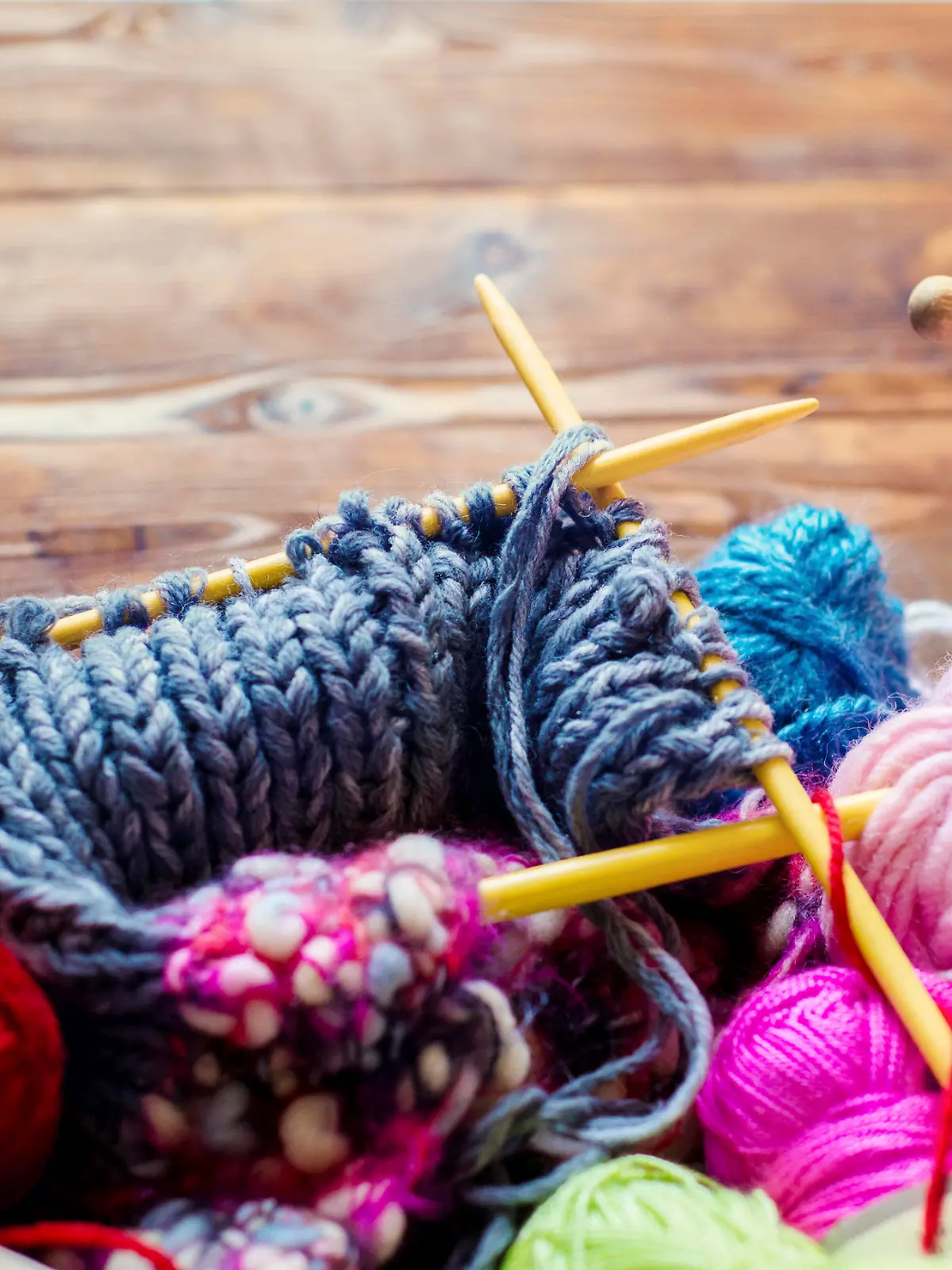 view from above on a wooden table with lots of balls of wool, knitting needles and other tools.  Place for text and the word craft