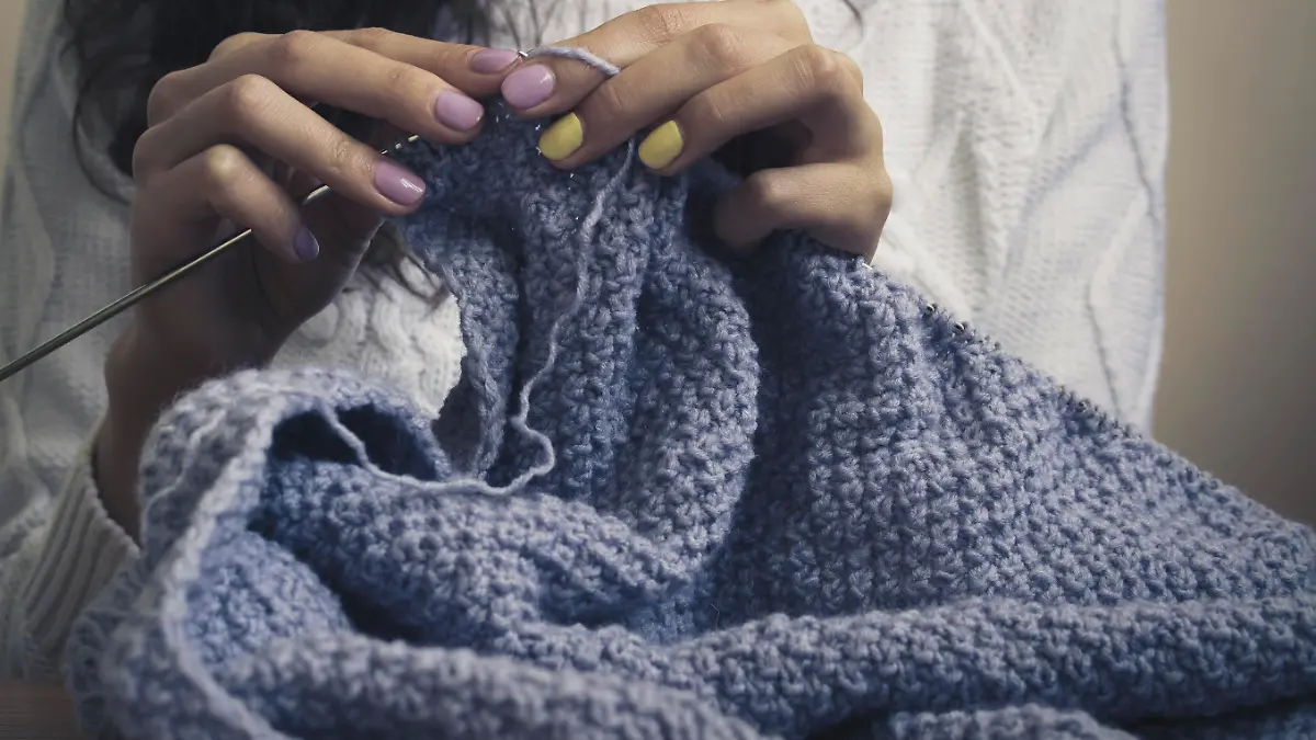 The girl in the white sweater with bright manicure knits blue thread. Vintage photo close up.