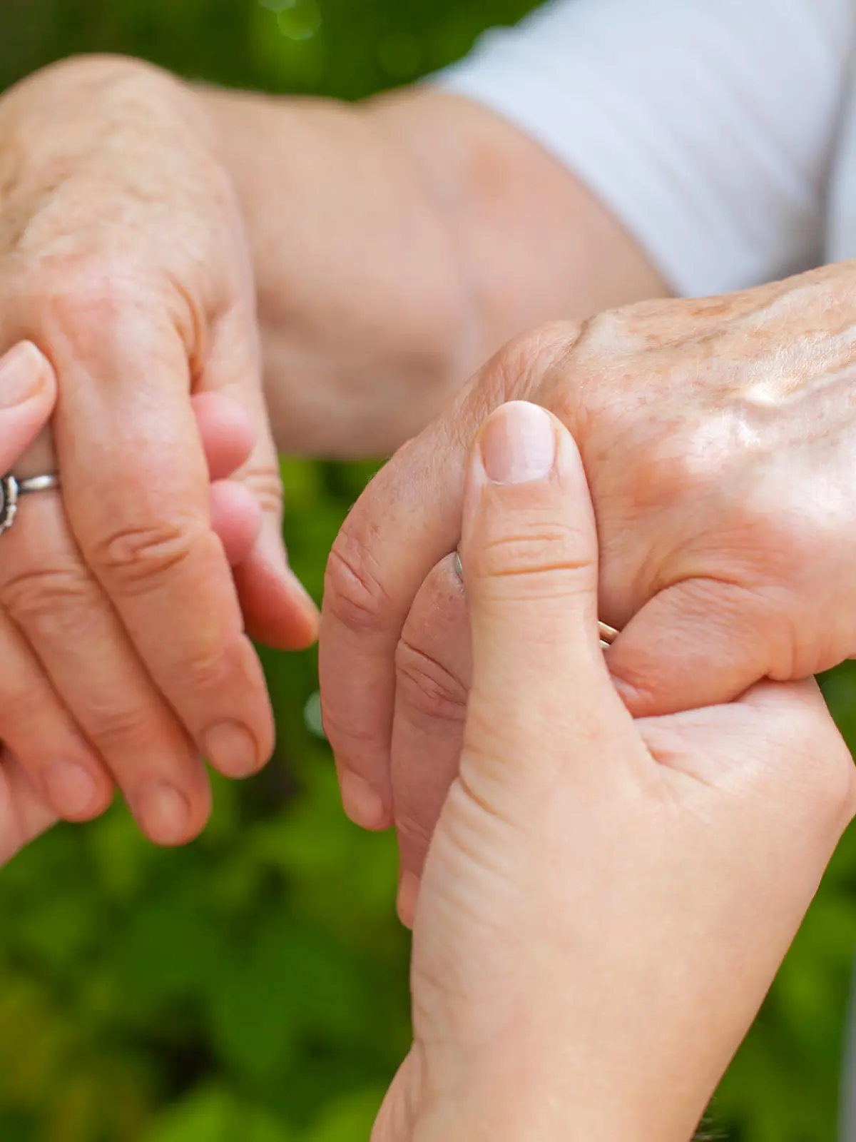 Close up young caregiver holding elderly female's trembling hands, Parkinson disease