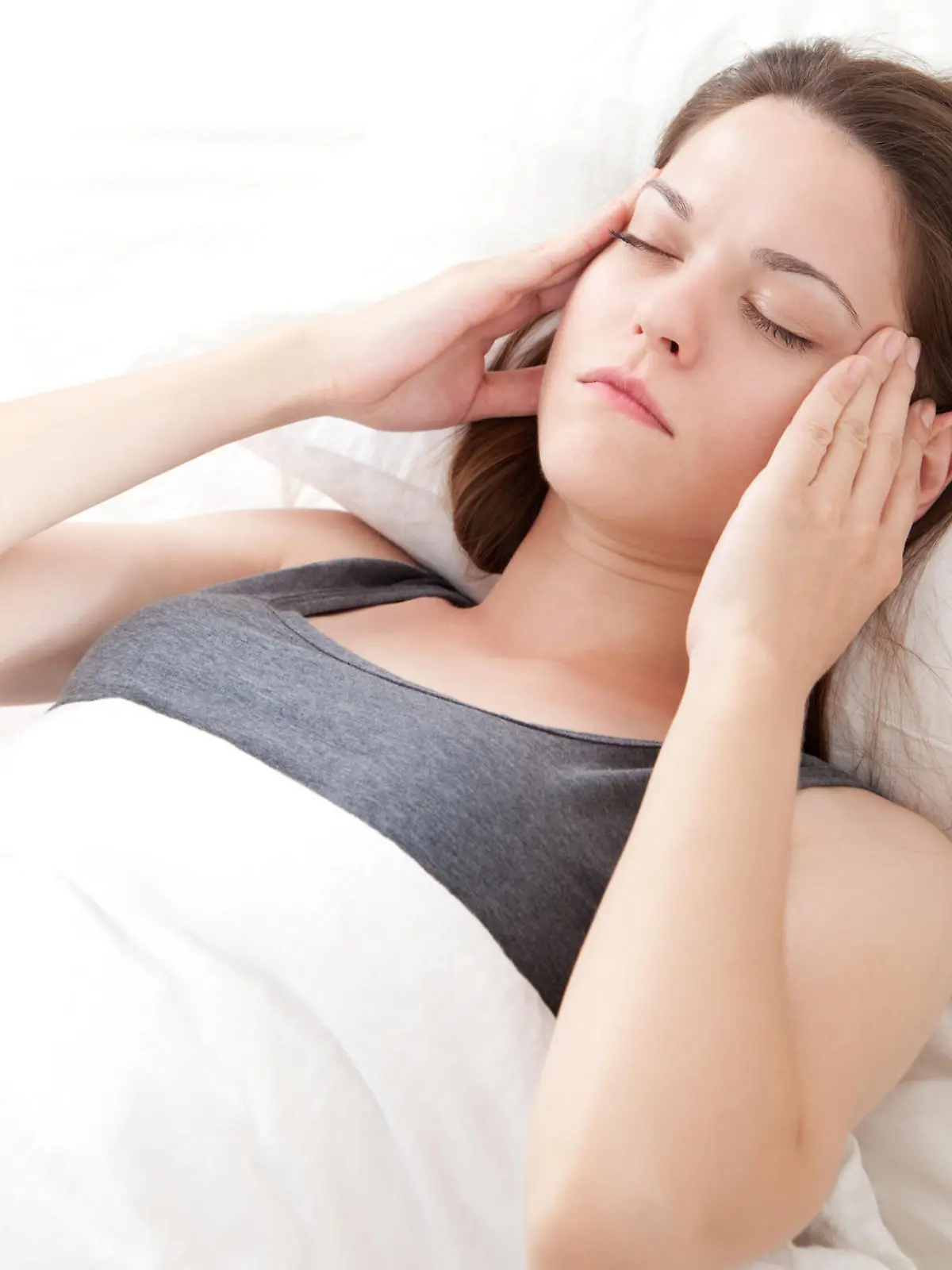 Beautiful young woman lying in bed and having migraine