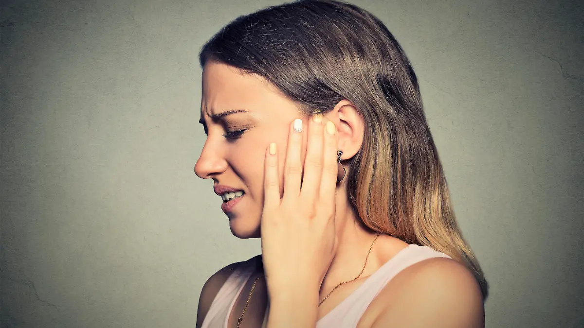 Tinnitus. Closeup side profile sick young woman having ear pain touching her painful head isolated on blue background