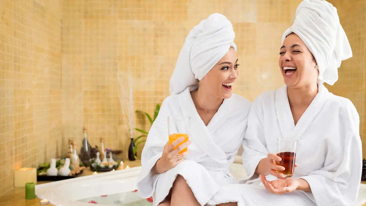 Cheerful women in bathrobes drinking juice: friends in spa salon
