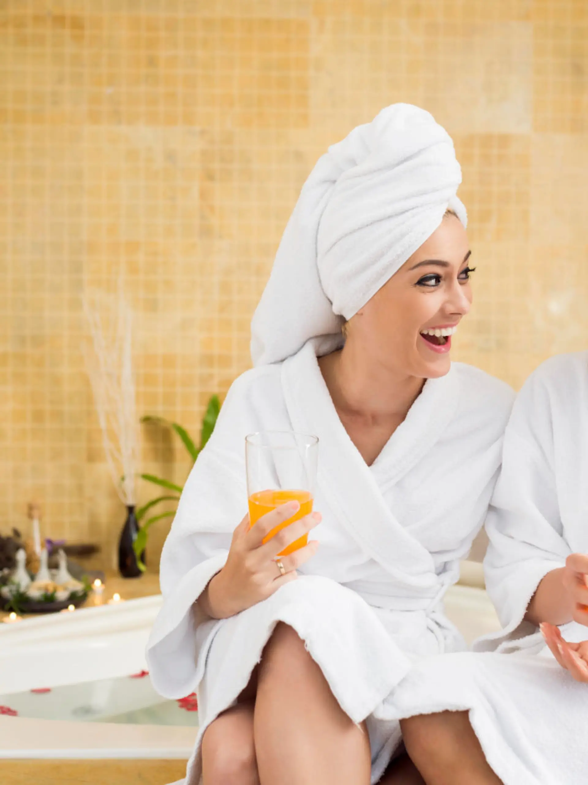 Cheerful women in bathrobes drinking juice: friends in spa salon