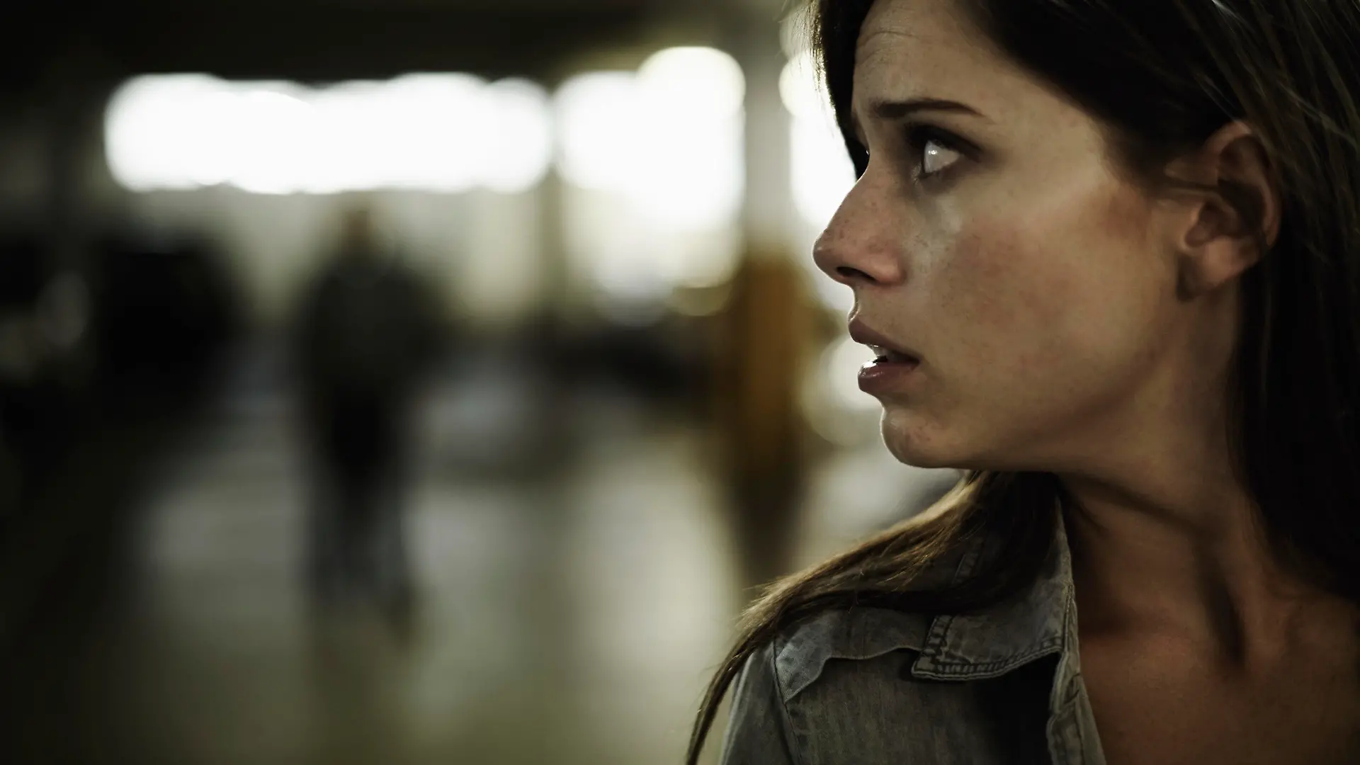 A terrified young woman in an underground parking garage being followed by a sinister man