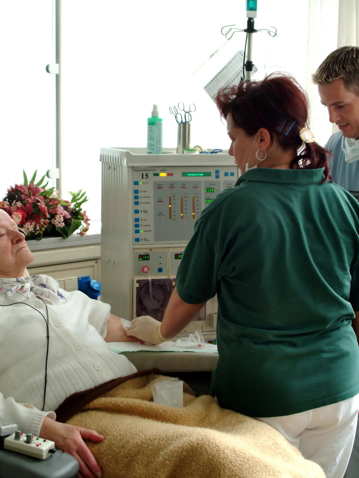 Zwei Arzthelfer schliessen eine Patientin für die Blutwäsche mit Schläuchen an ein Dialyse-Gerät an. Aufgenommen am 22.03.2004 in einer Dialysepraxis in Iserlohn. Ein wesentlicher Teil ihres Lebens ist für Patienten, die an einer Niereninsuffizienz erkrankt sind, die Dialyse. Zwei bis dreimal in der Woche müssen sie sich für fünf Stunden einer Blutwäsche unterziehen, da ihre Nieren diese Funktion nicht mehr gewährleisten. Zuwendung von Arzt und Arzthelferinnen sowie dem Dialysekrankenpfleger sind da besonders wichtig. Foto: Klaus Rose +++(c) dpa - Report+++ | Verwendung weltweit