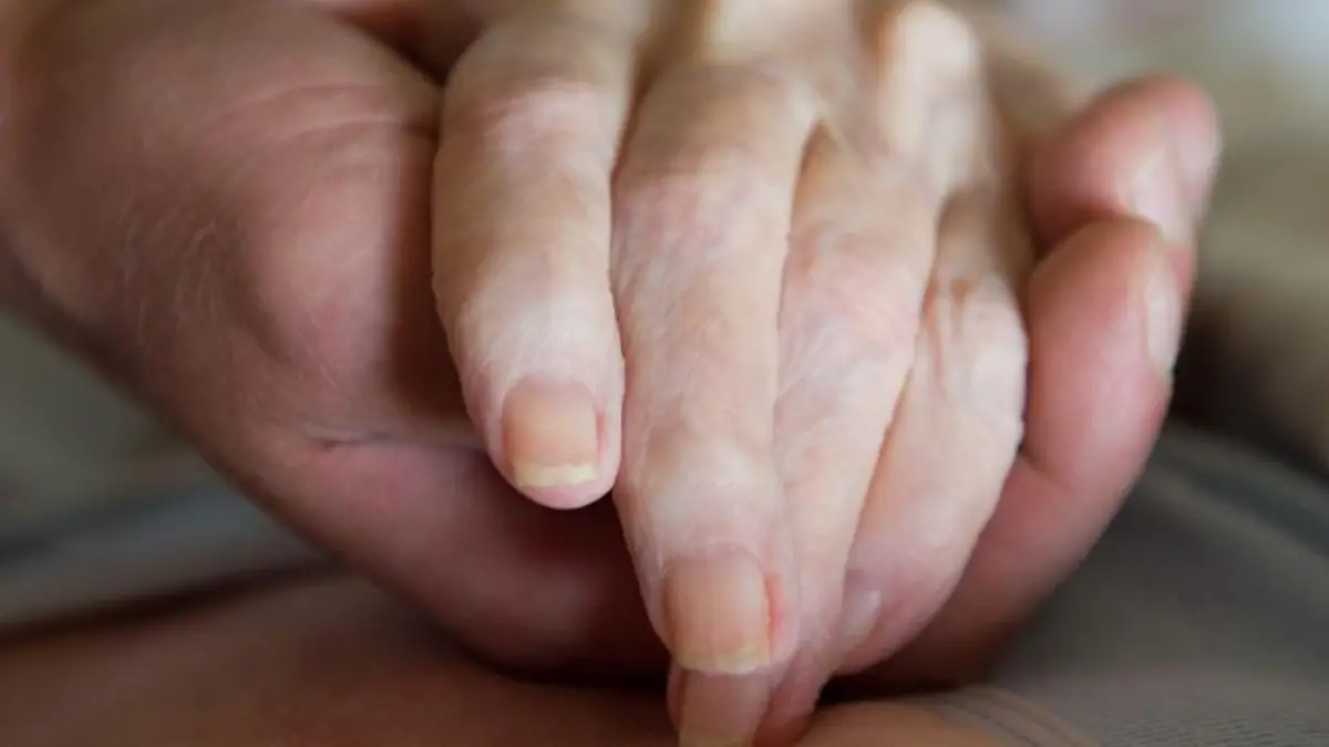 Ein Pfleger hält die Hand einer alten Frau