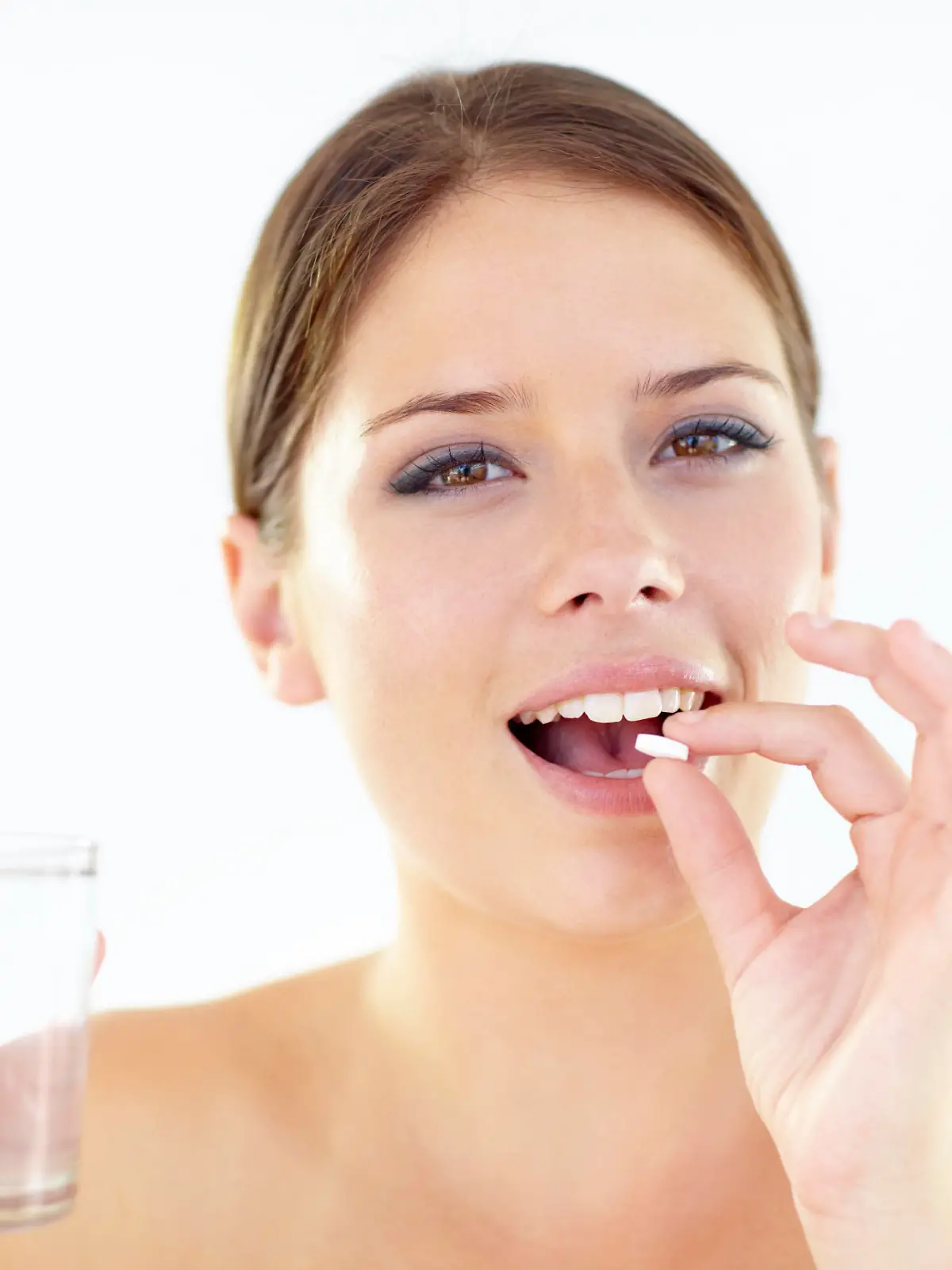 Smiling young woman isolated on white while taking a pill and holding a glass of water