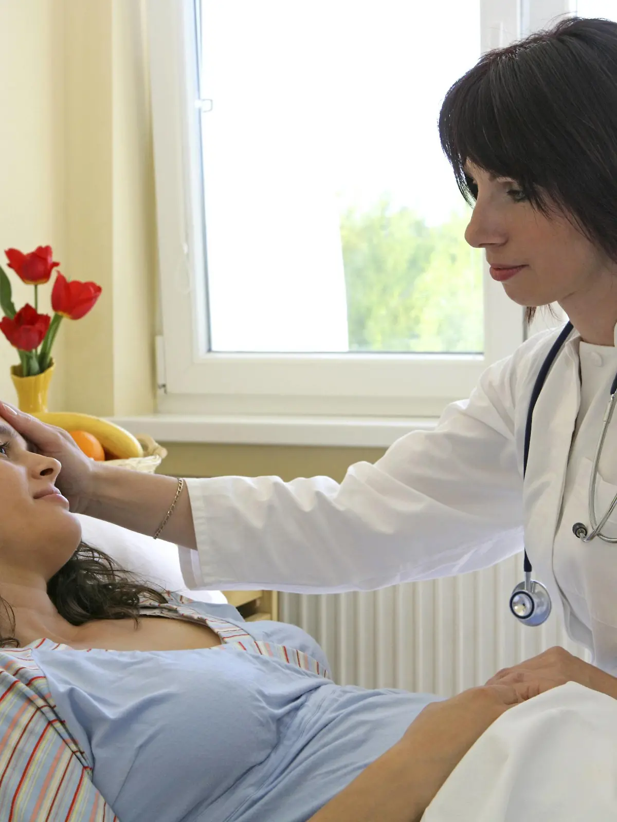 Krankenhausaerztin untersucht Schwangere, legt die Hand auf die Stirn, Deutschland | doctor checking pregnant woman, lying on hospital bed, Germany