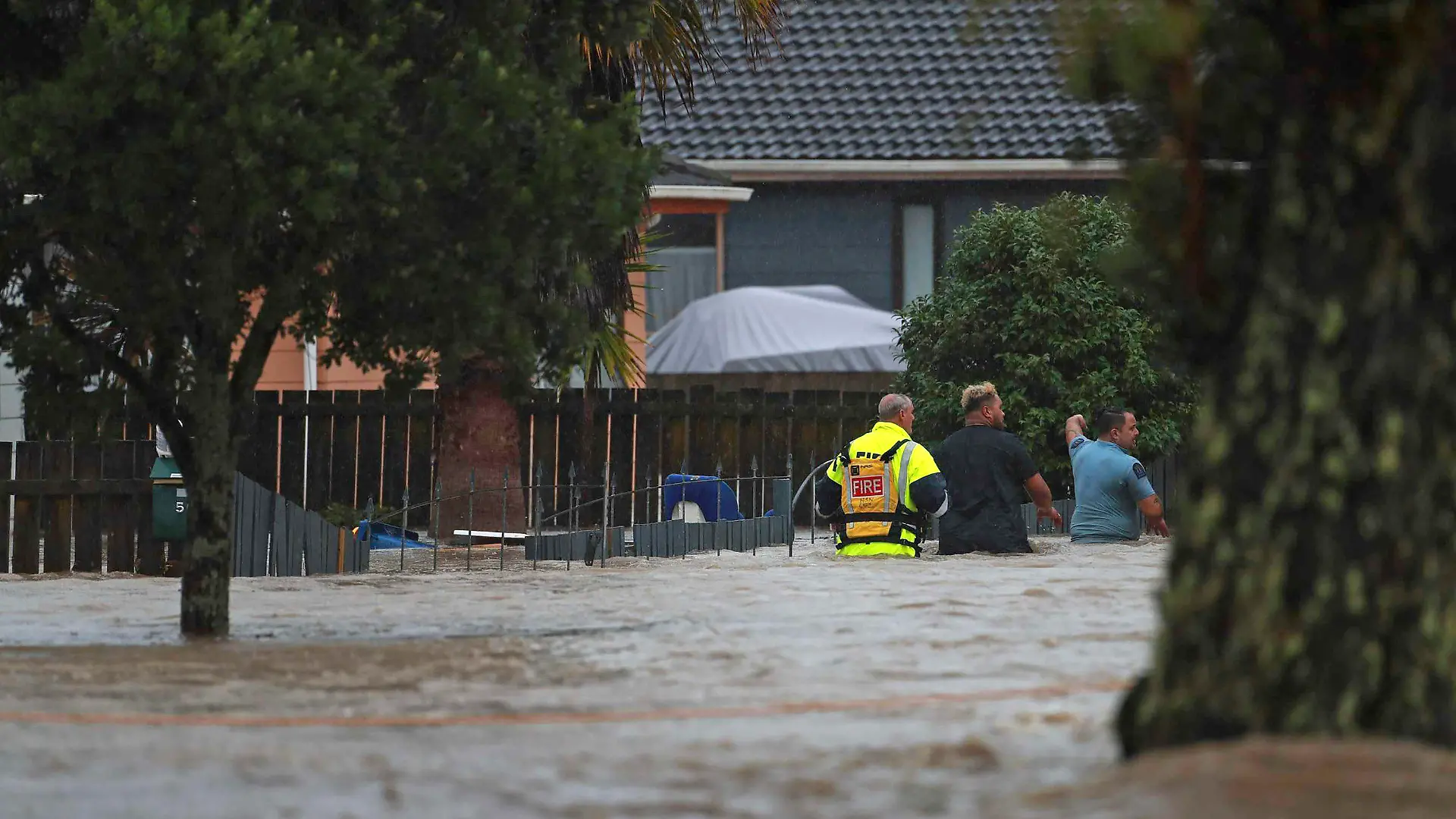 Emergency workers and a man wade through flood waters in Auckland, New Zealand, Friday, Jan. 27, 2023. Torrential rain and wild weather in Auckland causes disruptions throughout the city and an Elton John concert to be canceled just before it was due to start. (Hayden Woodward/New Zealand Herald via AP)