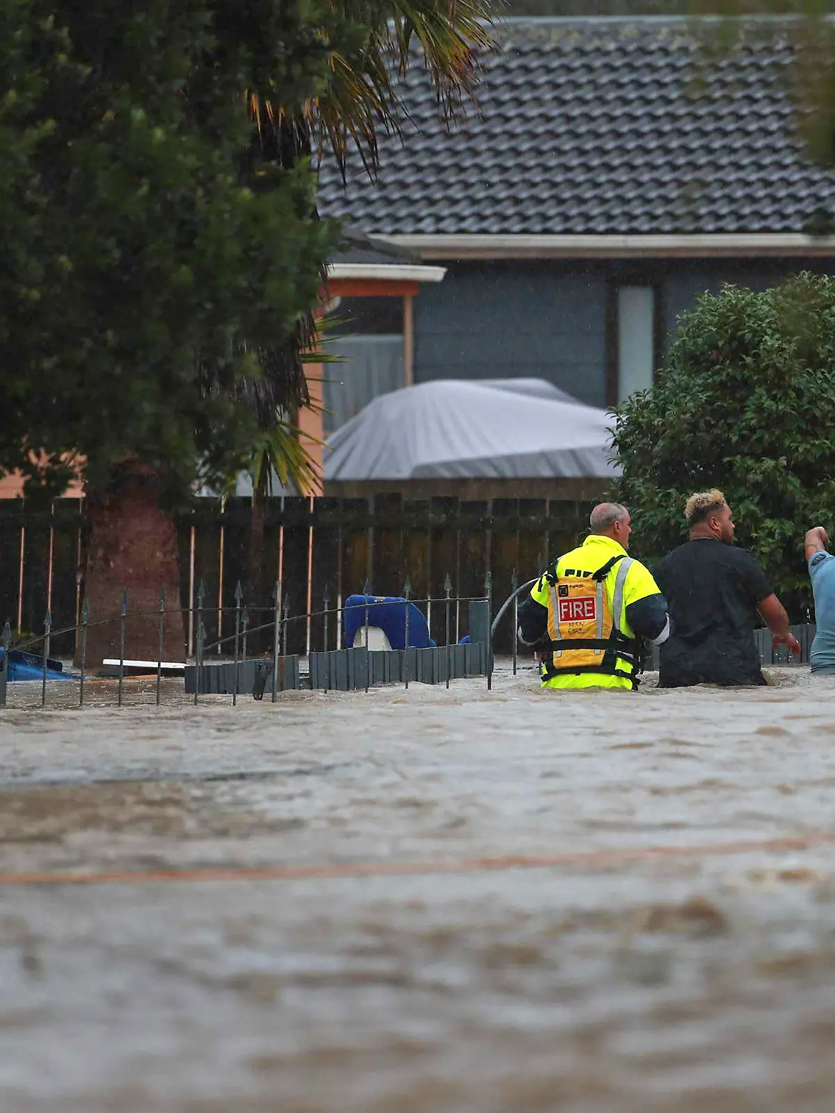 Emergency workers and a man wade through flood waters in Auckland, New Zealand, Friday, Jan. 27, 2023. Torrential rain and wild weather in Auckland causes disruptions throughout the city and an Elton John concert to be canceled just before it was due to start. (Hayden Woodward/New Zealand Herald via AP)
