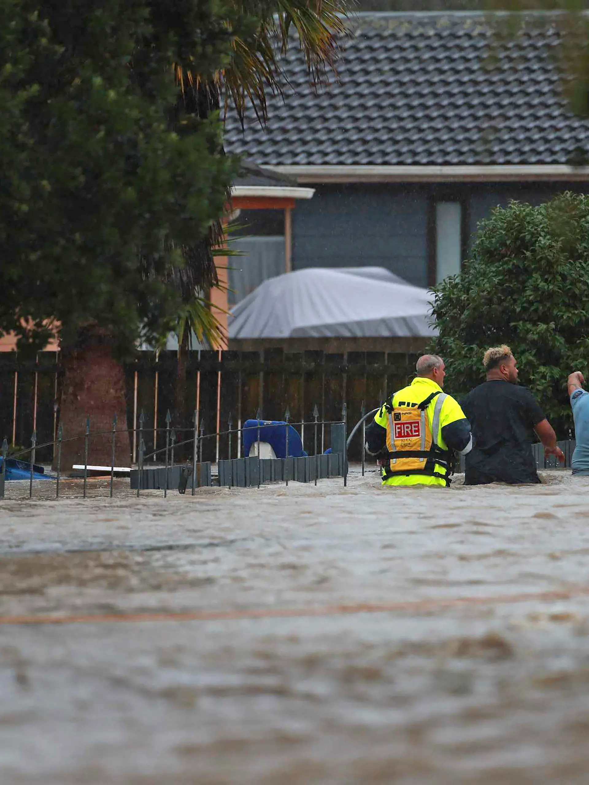 Emergency workers and a man wade through flood waters in Auckland, New Zealand, Friday, Jan. 27, 2023. Torrential rain and wild weather in Auckland causes disruptions throughout the city and an Elton John concert to be canceled just before it was due to start. (Hayden Woodward/New Zealand Herald via AP)
