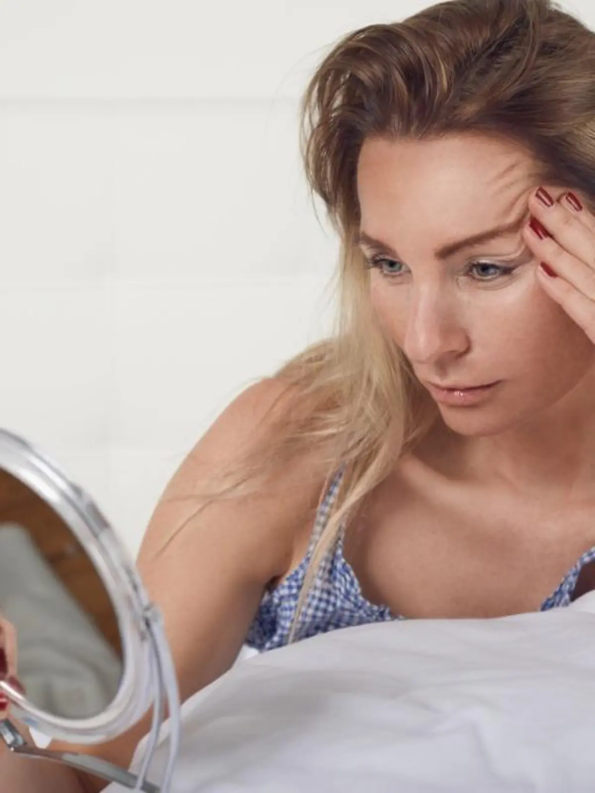 woman-looking-in-the-mirror-at-her-facial-wrinkles-picture-id892694038