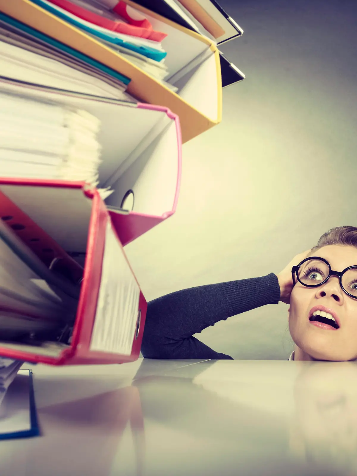 A lot of work and overwork concept. Terrified young businesswoman secretary with huge stack of binders. Scared accountant surrounded of to much work to do.